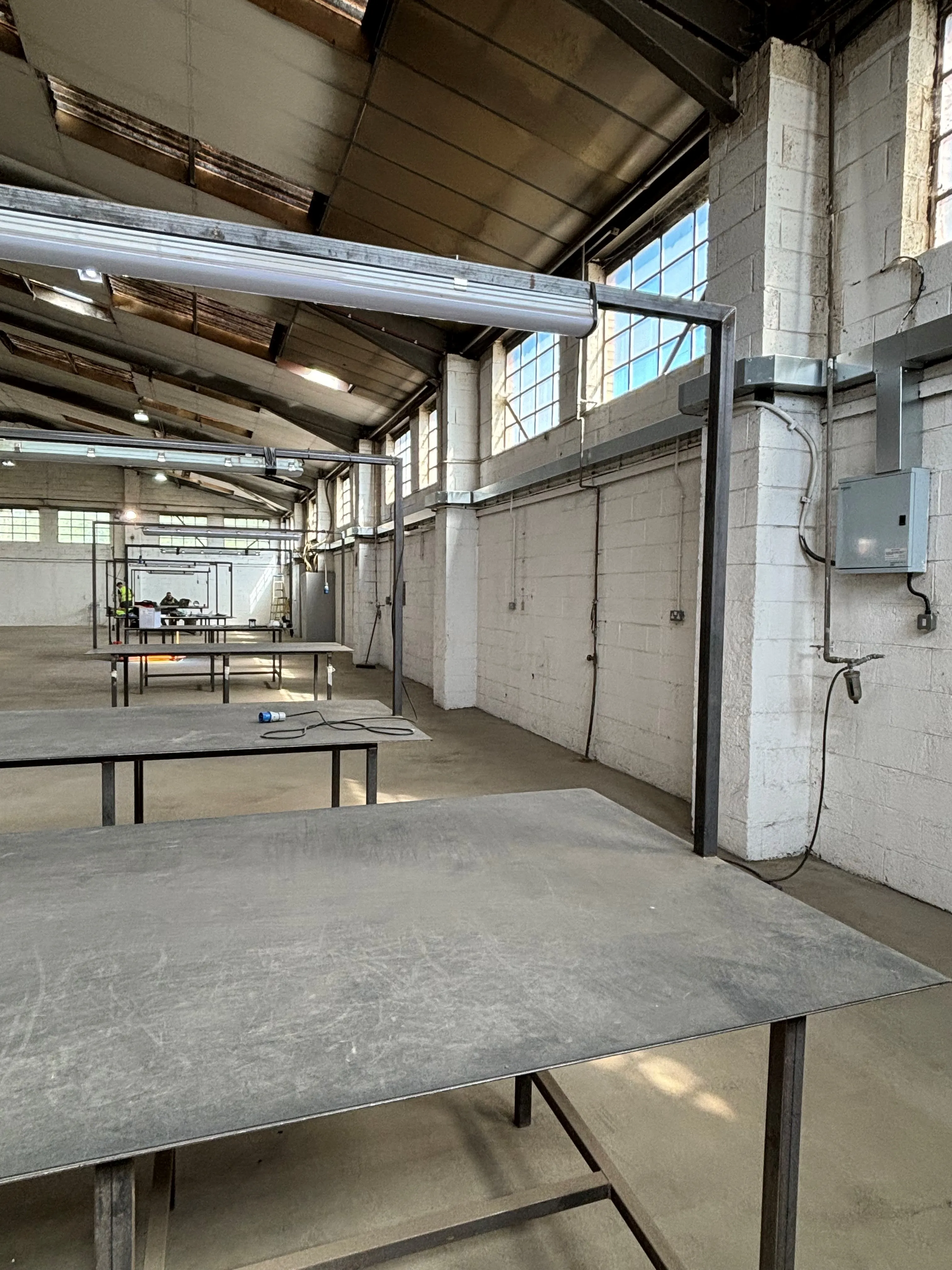 tables in a warehouse with a ceiling of windows and a wall