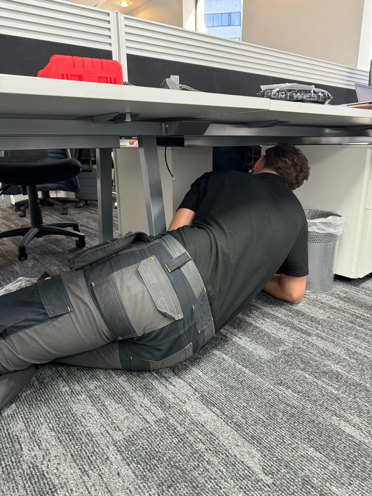 there is a man that is laying on the floor under a desk