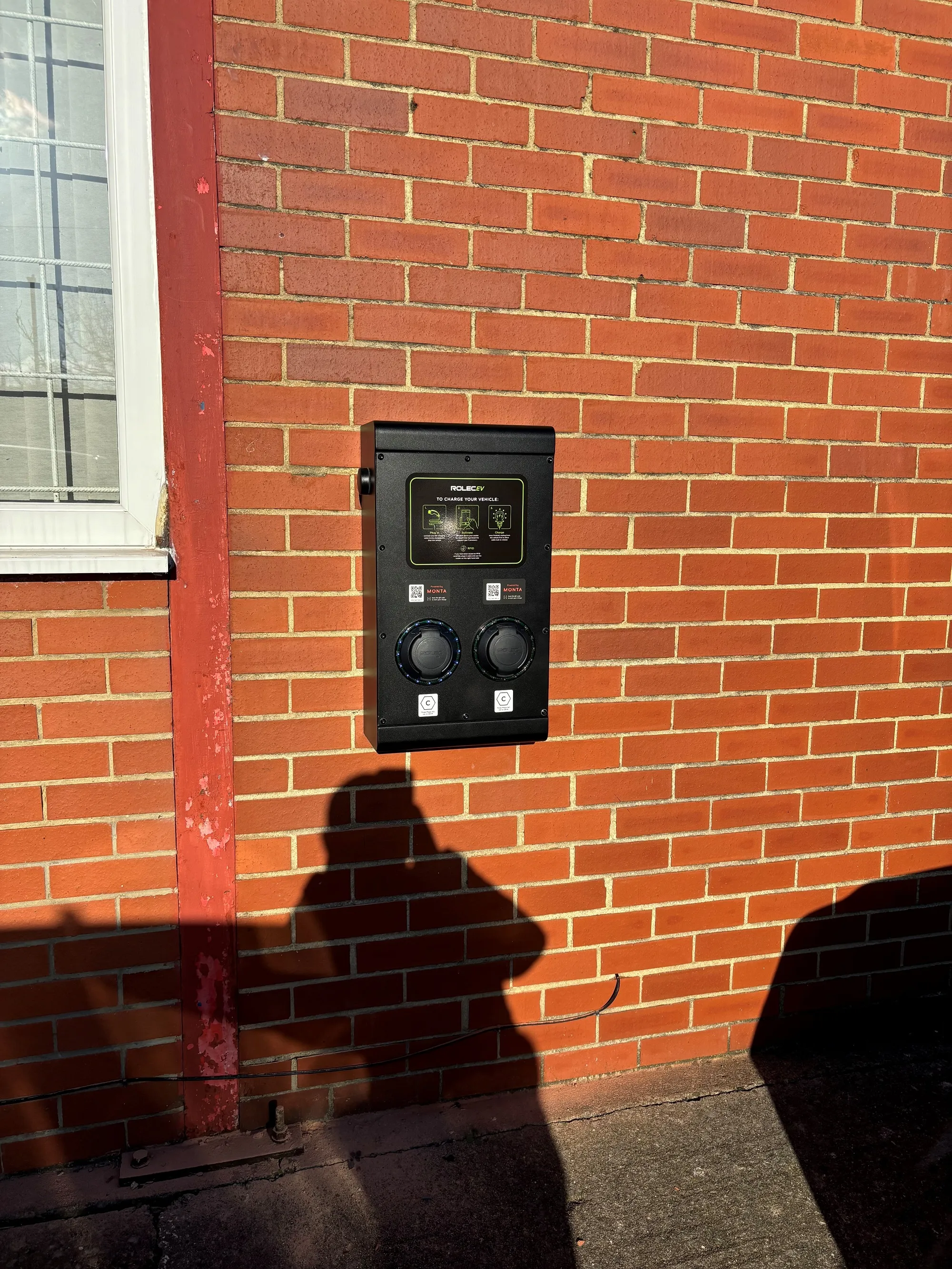 A shadow of a person standing next to a brick building.
